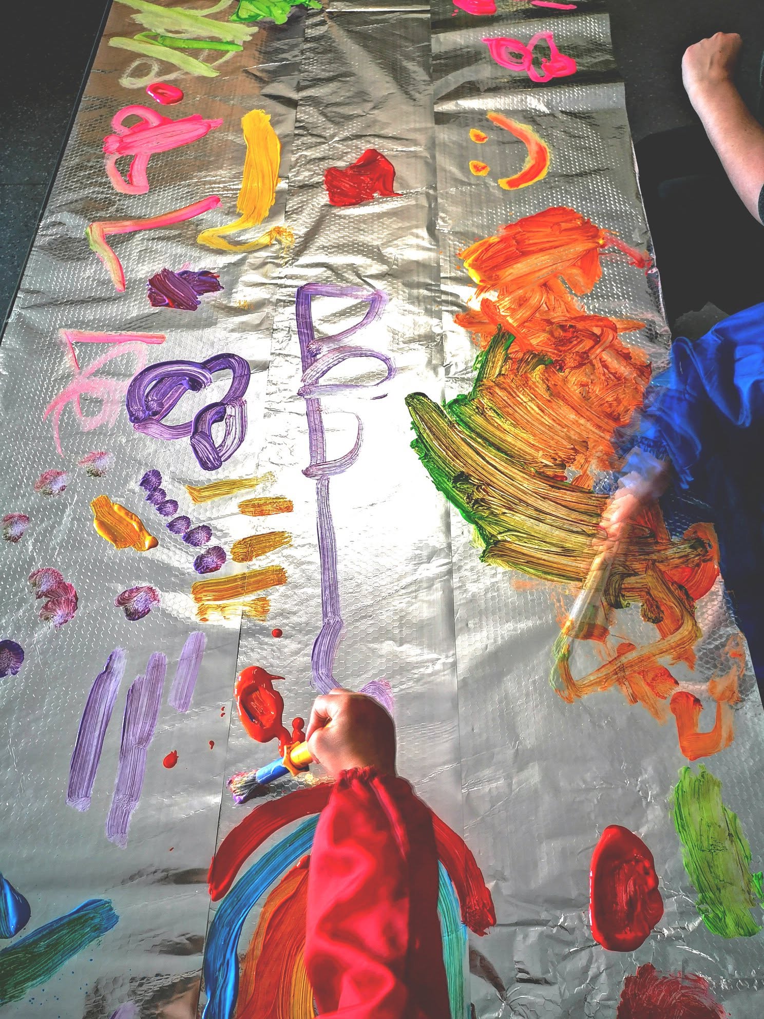 Children painting colourful marks on a large shiny sheet