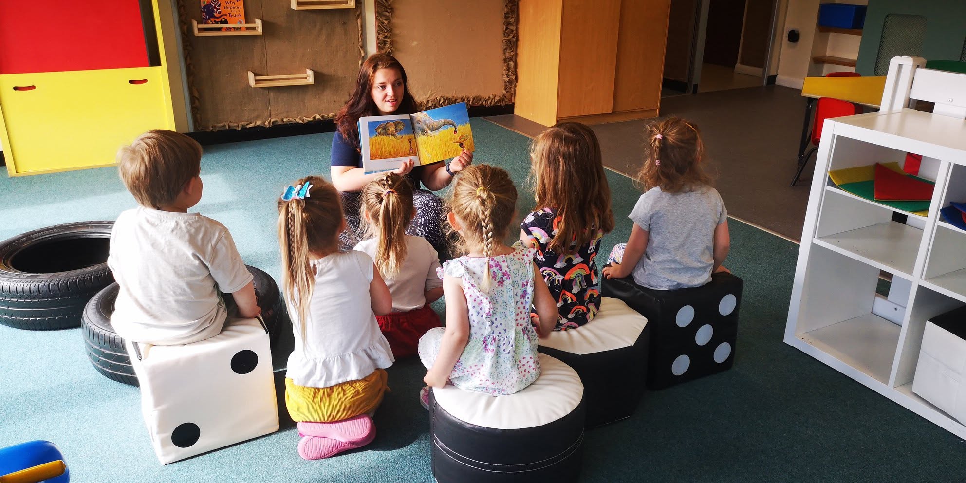 Children sitting in a circle while a nursery practitioner reads a picture book