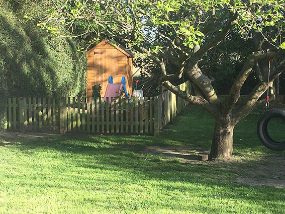 The wooden playhouse behind a picket fence in the Wymondham garden