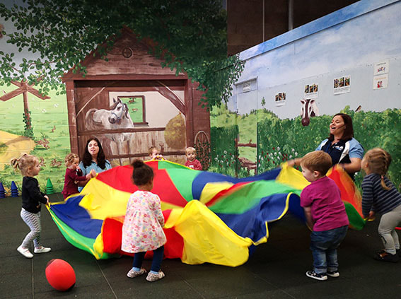 Children and nursery practitioners enjoying colourful parachute play in the Garden Room